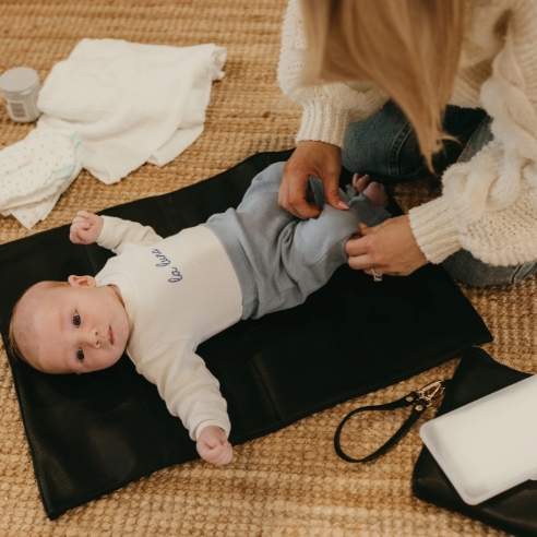 Mum changing a baby on the changemat from the nappy pouch in black