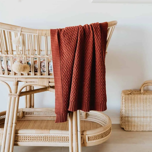 Rust diamond baby blanket hanging over bassinet