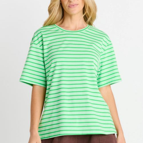 A woman modeling a green and white horizontally striped short-sleeve t-shirt with brown shorts, set against a plain light gray studio background.