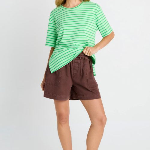 A woman modeling a green and white striped short-sleeve t-shirt and brown shorts against a light gray studio background.