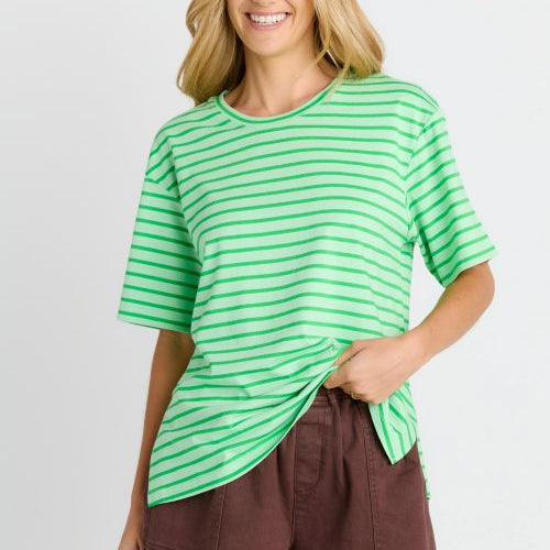 A woman modeling a bright green short-sleeve t-shirt with thin white horizontal stripes, paired with brown shorts, against a light gray studio background.