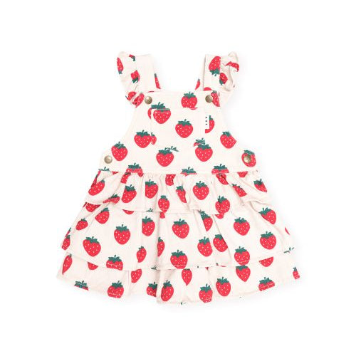 A baby girl's tiered overall dress featuring a red strawberry print on a warm cream background, with ruffled shoulder straps and a button closure.