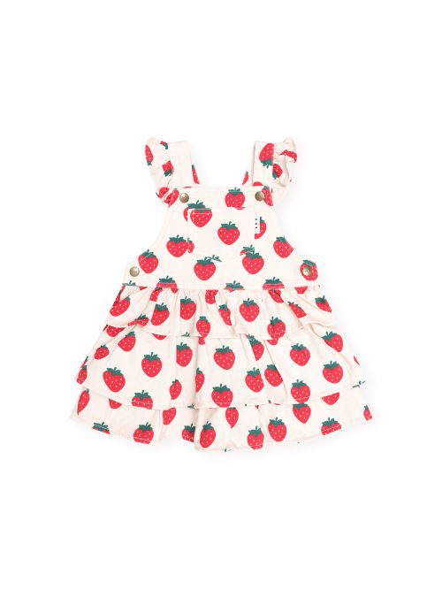 A baby girl's tiered overall dress featuring a red strawberry print on a warm cream background, with ruffled shoulder straps and a button closure.