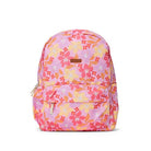 A pink backpack with a vibrant floral print in shades of orange, yellow, and red, featuring a front zippered pocket and a small brown leather brand patch.