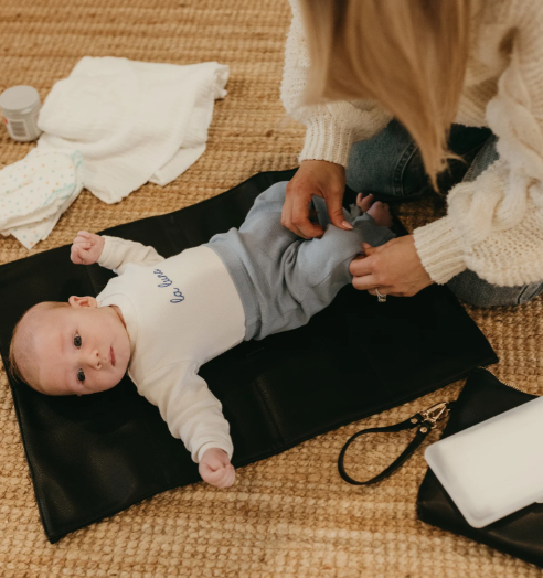 Mum changing a baby on the changemat from the nappy pouch in black