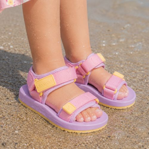 Pair of beach sandals in sugar plum on a childs feet in the sand