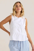 Woman wearing a white sleeveless top and blue striped pants against a plain background