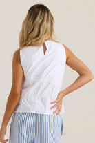 Woman wearing a white sleeveless top and blue striped pants against a plain background