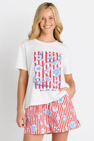 A woman modeling a white graphic t-shirt and matching red, white, and blue striped swim shorts against a plain white background.