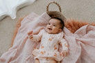 Baby in a moses basket wearing a onesie flutter dress in classic fawn