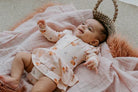 Baby in a moses basket wearing a onesie flutter dress in classic fawn