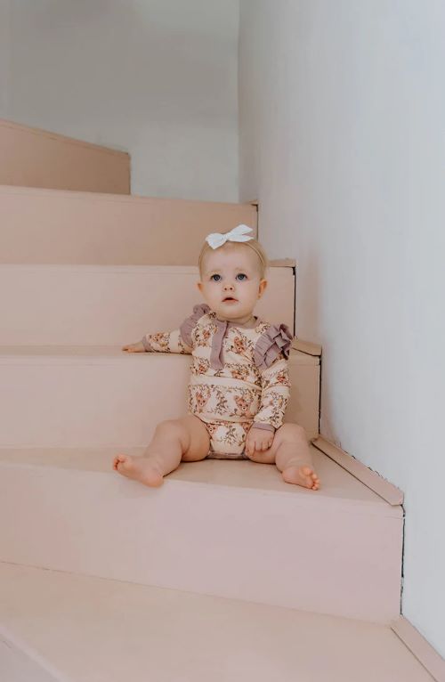 Toddler sitting on steps wearing frilly bodysuit in vintage teddies print