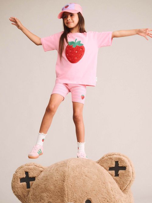 girl standing on a bear wearing the strawberry slouchy tee