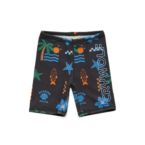 A pair of kids' swim trunks by Cruwolf, featuring a black base with a colorful tropical beach print including palm trees, starfish, fish, and 'Seaside Motel' text, with the brand name 'CRUWOLF' printed vertically on the right leg.