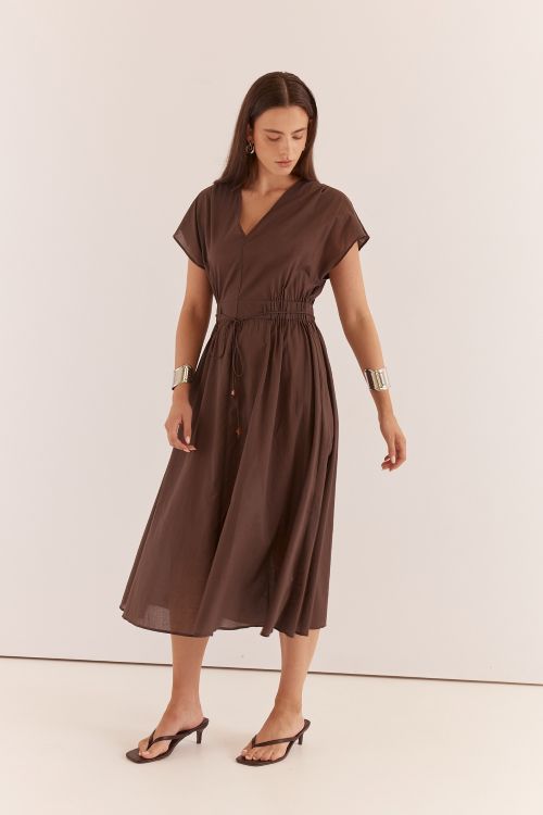A woman modeling a brown midi wrap dress with short sleeves, a V-neckline, and a gathered waist with front buttons, photographed against a plain off-white studio background.