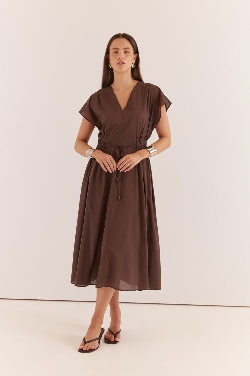 A woman modeling a brown midi wrap dress with short sleeves, a V-neckline, and a drawstring waist, set against a plain off-white studio background.
