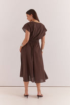 A woman wearing a dark brown midi dress with flutter sleeves and a gathered waist, shown from the back against a plain light background.