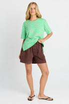 A woman modeling a green and white striped short-sleeve t-shirt and brown shorts against a light gray studio background.