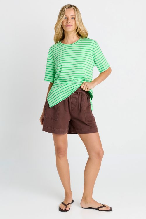 A woman modeling a green and white striped short-sleeve t-shirt and brown shorts against a light gray studio background.