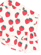 A close-up of a ruffled skirt with a red strawberry print on a cream background, featuring button details and pockets.