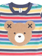 A close-up of a children's striped long-sleeve top with a large brown teddy bear face applique on the front. The shirt features horizontal stripes in navy blue, red, yellow, green, and white, with a navy collar and a white tag reading 'XUX' inside the neck.